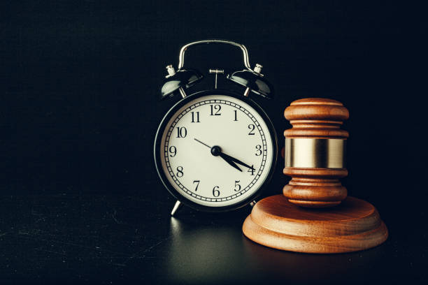 A silver bell alarm clock stands next to a wooden court gavel.