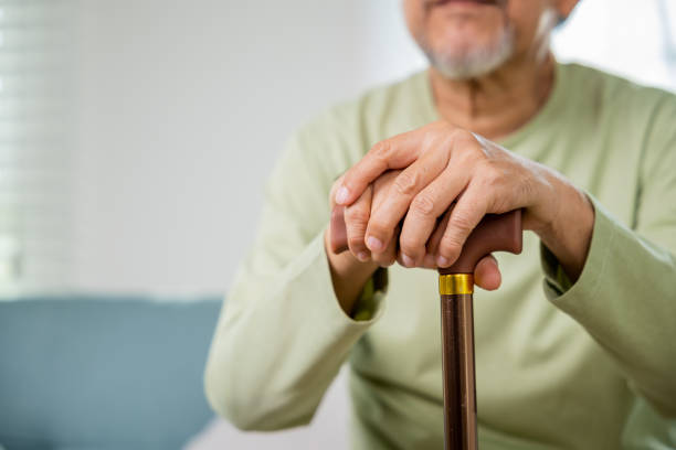 An older man sitting down with hands folded on top of a cane.